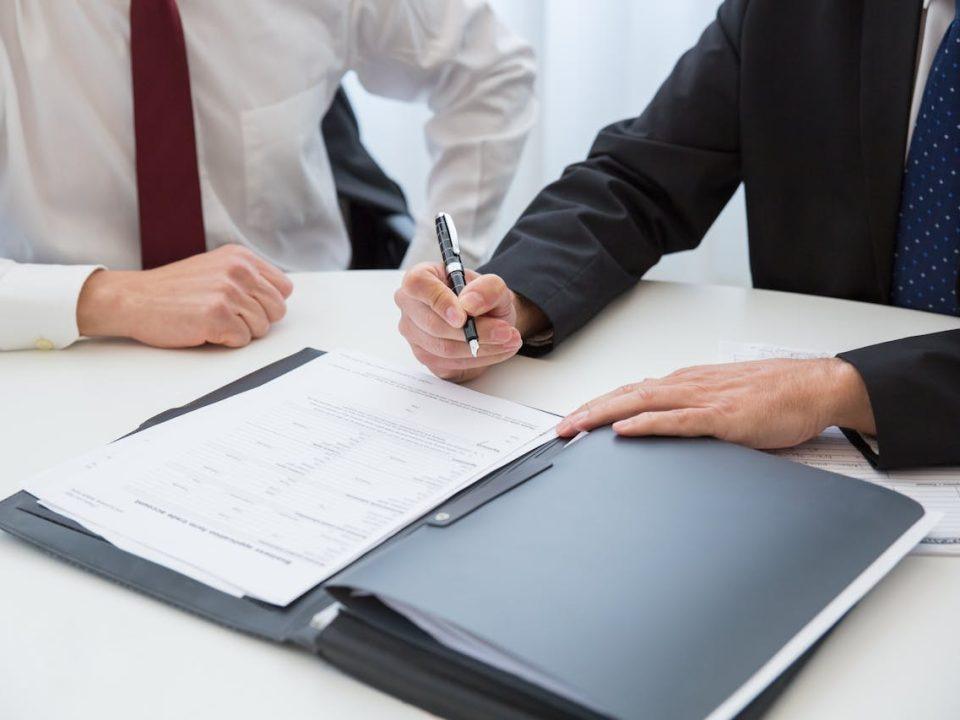 Business professionals reviewing and signing legal and administrative documents at a desk.