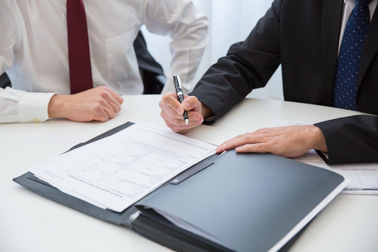 Business professionals reviewing and signing legal and administrative documents at a desk.
