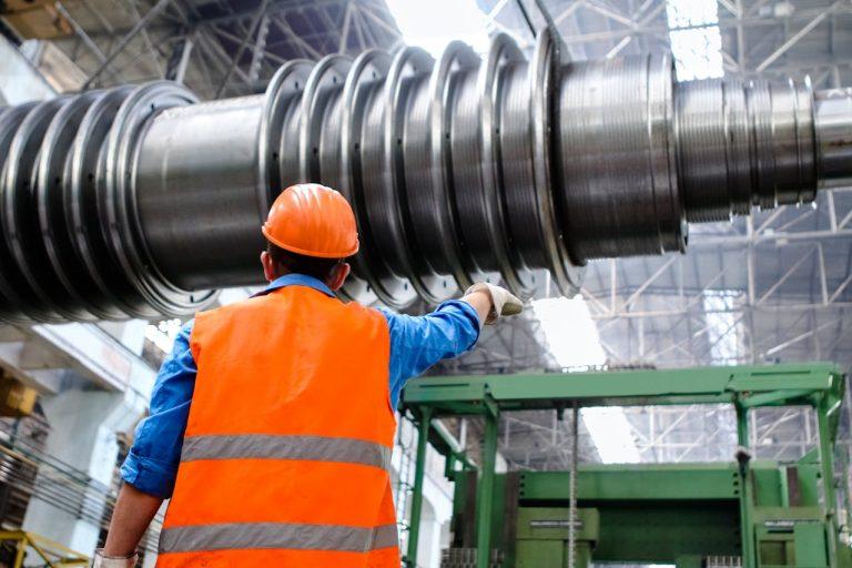 Industrial worker wearing safety gear inspecting large rotating machinery inside a manufacturing plant.