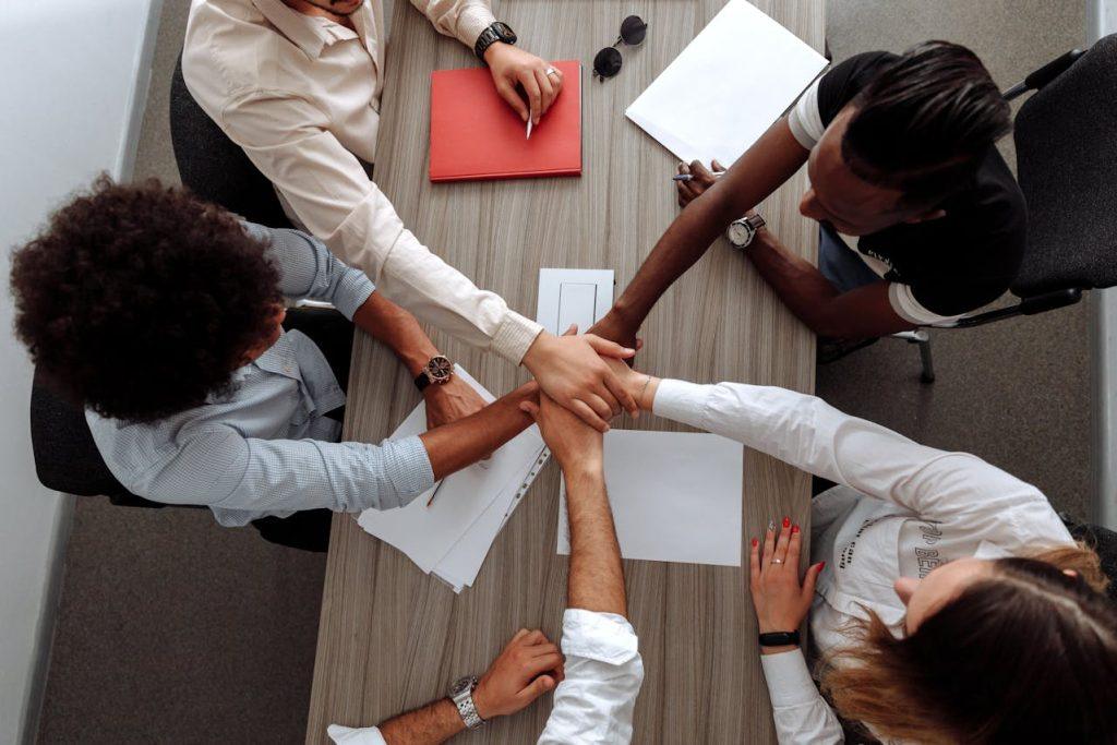 Diverse team placing hands together in office meeting, symbolizing collaboration, teamwork, and modern workforce strategy